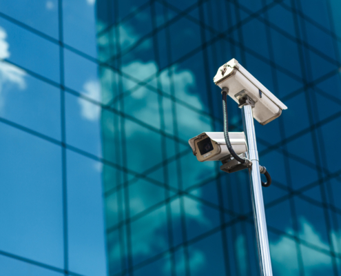 Side view of two surveillance cameras on a pole in the foreground, large skyscraper building in the background